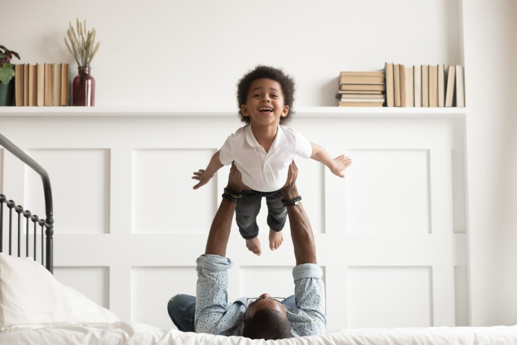 Happy funny african american kid boy flying in fathers arms