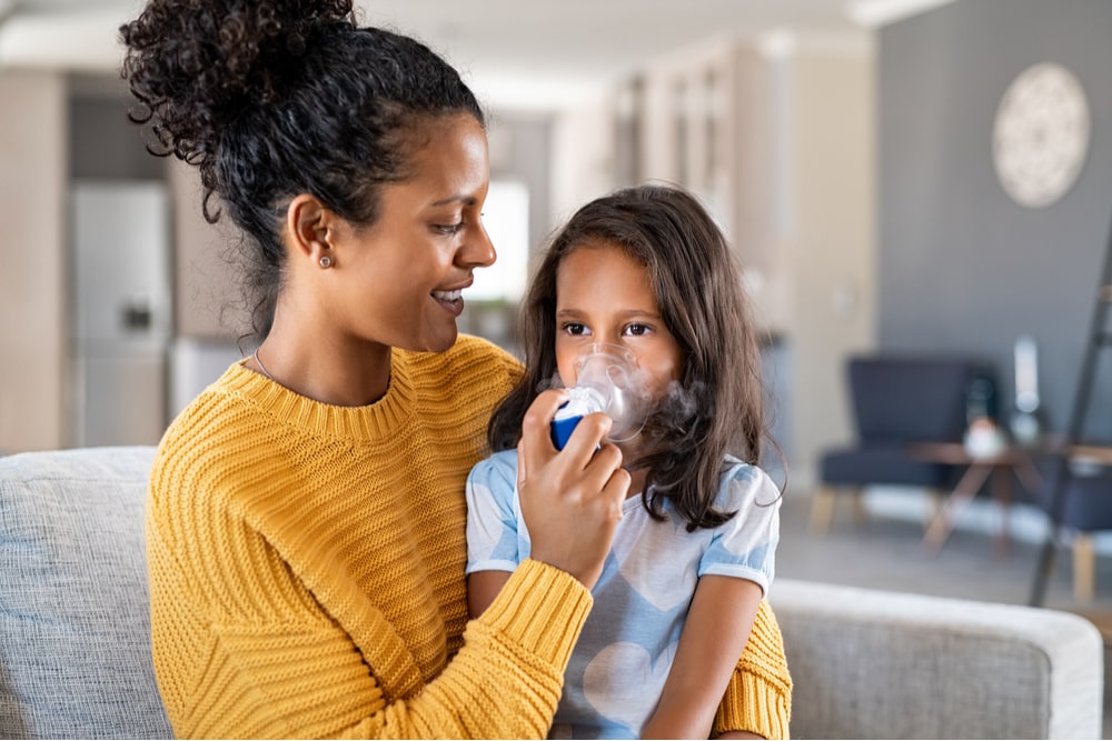 Little indian girl making inhalation with nebulizer with lovely mother.