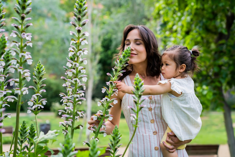 Side view of relaxed mother with active child in hands smelling flowers